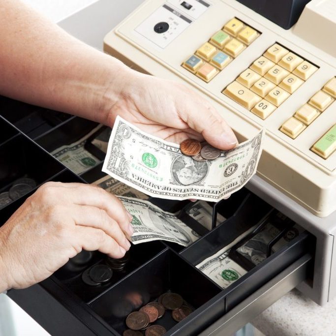 Horizontal view of an open cash register drawer asa a cashier makes change.